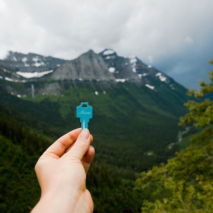 Clé turquoise tenue devant une vallée montagneuse verdoyante sous un ciel nuageux.